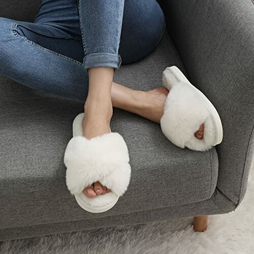 Person wearing fuzzy white slippers on a gray sofa