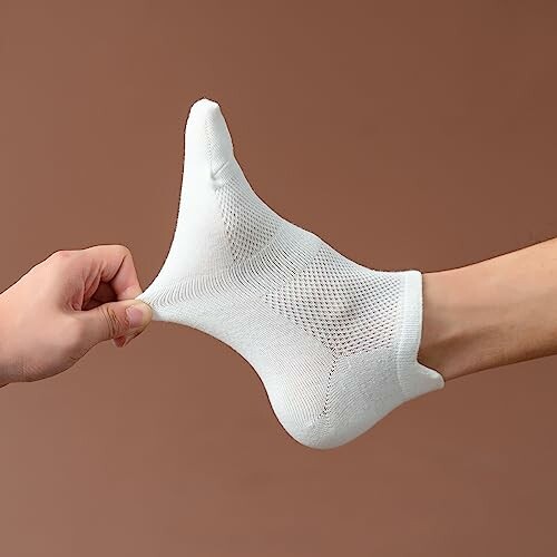 Hand stretching a white sock on a foot against a brown background.